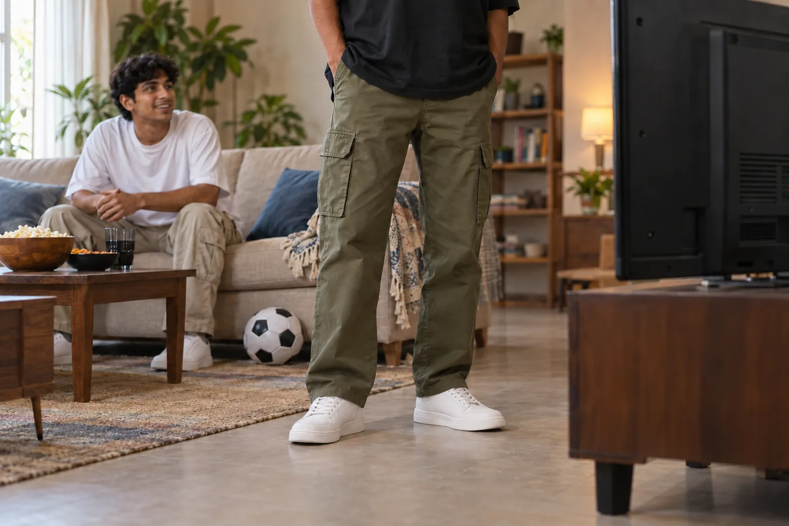 Olive cargo trouser hems resting above trainers as friends gather to watch a match